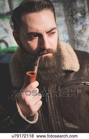 Stock Photo - Young bearded man smoking pipe by graffiti wall. Fotosearch