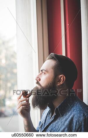 Young bearded man smoking pipe by window View Large Photo Image Stock Image - Young bearded man smoking pipe by window. Fotosearch