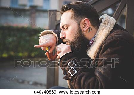 Stock Photo - Young bearded man smoking pipe on steps. Fotosearch
