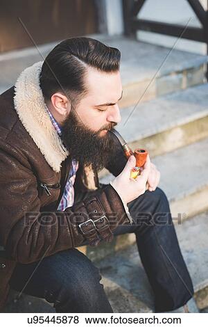 Stock Photo - Young bearded man smoking pipe on steps. Fotosearch