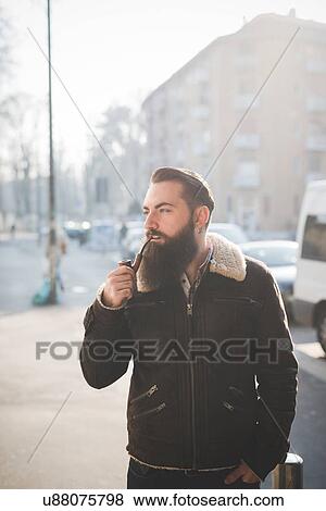 Stock Photo - Young bearded man smoking pipe on street. Fotosearch