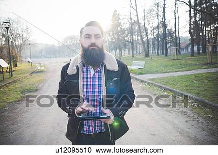 Young bearded man using digital tablet in park View Large Photo Image Stock Image - Young bearded man using digital tablet in park. Fotosearch