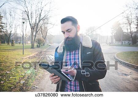 Young bearded man using digital tablet in park View Large Photo Image Stock Image - Young bearded man using digital tablet in park. Fotosearch