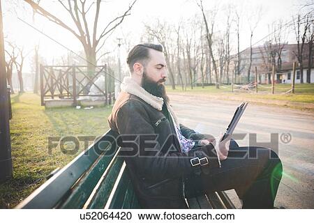Young bearded man using digital tablet on park bench View Large Photo Image Stock Image - Young bearded man using digital tablet on park bench. Fotosearch