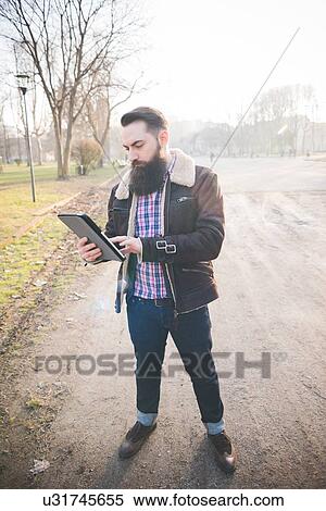 Young bearded man using digital tablet in park View Large Photo Image Stock Photography - Young bearded man using digital tablet in park. Fotosearch
