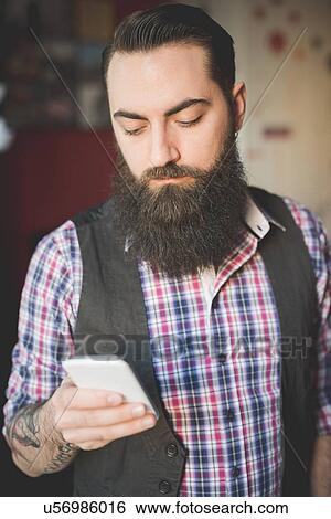 Young bearded man using smartphone in room View Large Photo Image Stock Photograph - Young bearded man using smartphone in room. Fotosearch