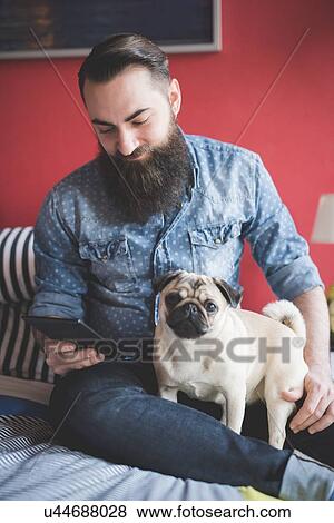 Stock Photo - Young bearded man using smartphone on bed. Fotosearch