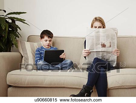 Stock Photography - "Young boy using digital tablet, mother reading newspaper". Fotosearch