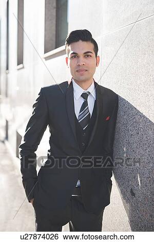 Stock Photograph - Young businessman leaning against wall. Fotosearch