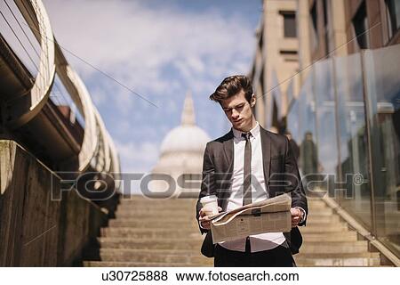 Young businessman reading newspaper walking down city stairway View Large Photo Image Stock Photo - Young businessman reading newspaper walking down city stairway. Fotosearch