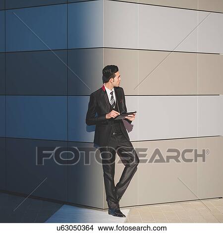 Picture - Young businessman using digital tablet against wall. Fotosearch