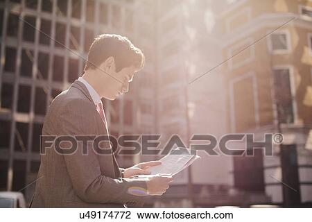 Young city businessman reading newspaper whilst walking View Large Photo Image Stock Image - Young city businessman reading newspaper whilst walking. Fotosearch