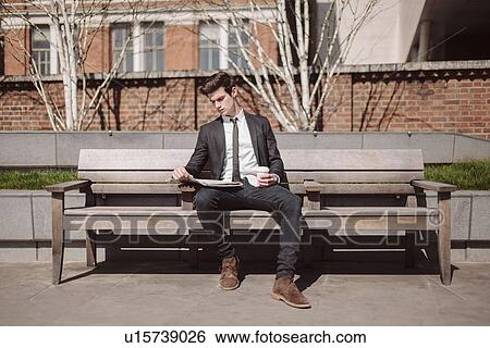 Young city businessman reading newspaper on bench View Large Photo Image Stock Photograph - Young city businessman reading newspaper on bench. Fotosearch