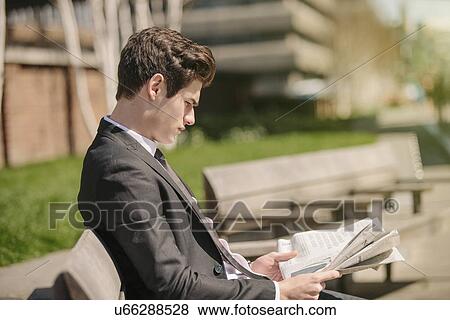 Young city businessman sitting on bench reading newspaper View Large Photo Image Stock Photo - Young city businessman sitting on bench reading newspaper. Fotosearch