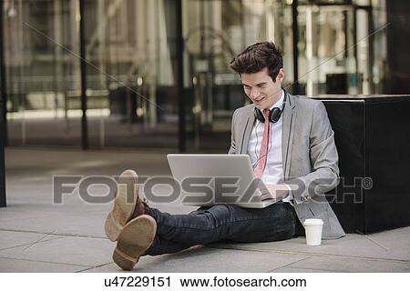 Young city businessman sitting on sidewalk using laptop View Large Photo Image Stock Image - Young city businessman sitting on sidewalk using laptop. Fotosearch