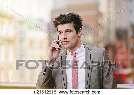 Stock Photography - Young city businessman talking on smartphone outside office. Fotosearch