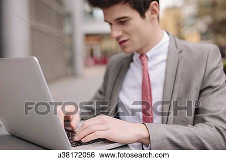 Young city businessman typing on laptop at sidewalk cafe View Large Photo Image Stock Photograph - Young city businessman typing on laptop at sidewalk cafe. Fotosearch