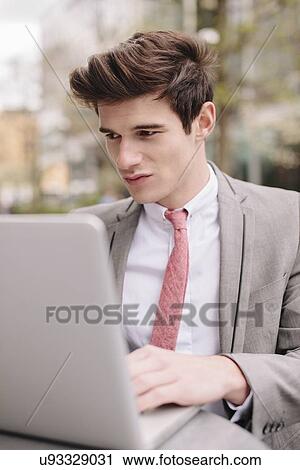 Stock Image - Young city businessman using laptop at sidewalk cafe. Fotosearch