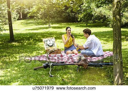 Young couple sitting eating picnic on blanket View Large Photo Image Stock Photo - Young couple sitting eating picnic on blanket. Fotosearch