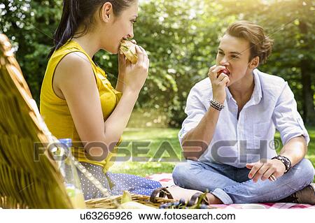 Stock Photograph - Young couple sitting eating picnic together. Fotosearch