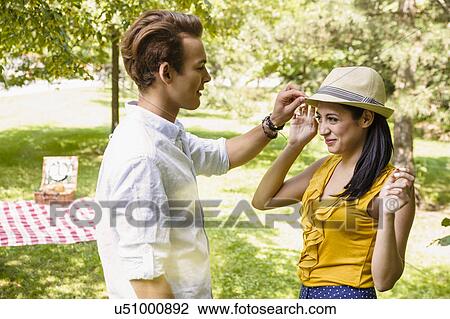 Stock Image - Young couple standing having fun with hat. Fotosearch