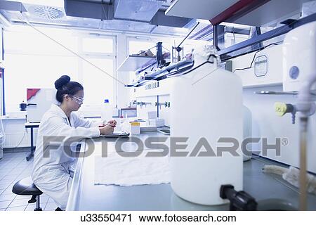 Stock Image - Young female scientist contemplating research notes on lab workbench. Fotosearch