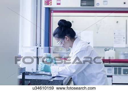 Stock Photo - Young female scientist in lab pipetting sample. Fotosearch