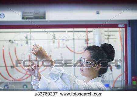 Stock Photo - Young female scientist pipetting sample into volumetric flask in lab. Fotosearch