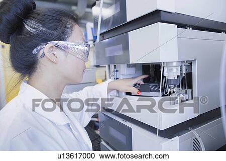 Stock Image - Young female scientist removing sample from equipment in lab. Fotosearch