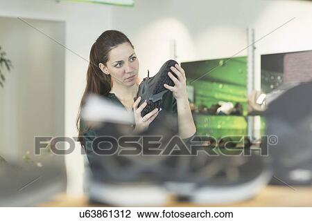 Young female shopper inspecting trainer in shoe shop View Large Photo Image Stock Image - Young female shopper inspecting trainer in shoe shop. Fotosearch