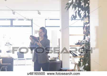 Stock Image - Young female shopper selecting sandal in shoe shop. Fotosearch