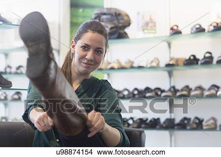 Young female shopper trying on knee length boot in shoe shop View Large Photo Image Picture - Young female shopper trying on knee length boot in shoe shop. Fotosearch