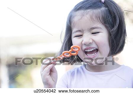 Stock Image - "Young girl blowing bubbles, laughing, close-up". Fotosearch