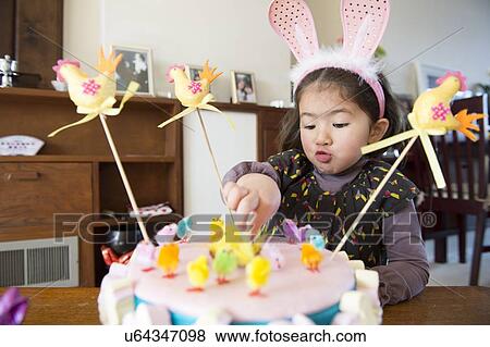 Stock Photo - "Young girl sitting at table, Easter cake in front of her". Fotosearch