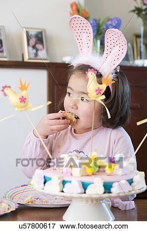 Stock Photo - "Young girl wearing bunny ears, eating cake". Fotosearch