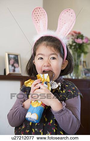 "Young girl wearing bunny ears, just about to bite into chocolate bunny" View Large Photo Image Stock Photo - "Young girl wearing bunny ears, just about to bite into chocolate bunny". Fotosearch