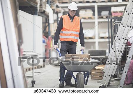 Young male warehouse worker pushing wheelbarrow in warehouse View Large Photo Image Stock Photo - Young male warehouse worker pushing wheelbarrow in warehouse. Fotosearch