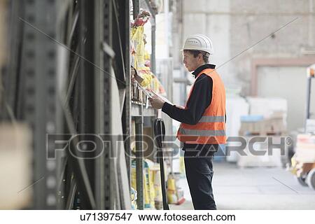 Young male warehouse worker searching shelves with clipboard in warehouse View Large Photo Image Stock Photo - Young male warehouse worker searching shelves with clipboard in warehouse. Fotosearch