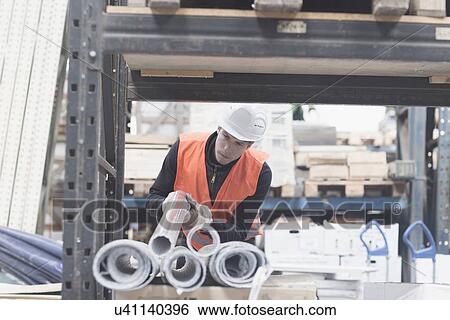 Stock Photograph - Young male warehouse worker selecting industrial pipe from shelf. Fotosearch