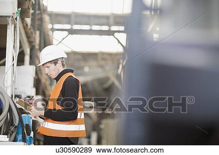 Stock Photo - Young male warehouse worker stock taking in warehouse. Fotosearch