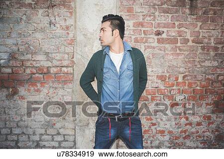 Stock Photo - Young man standing against brick wall. Fotosearch