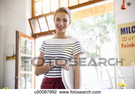 Stock Image - Young waitress holding tray smiling at camera. Fotosearch