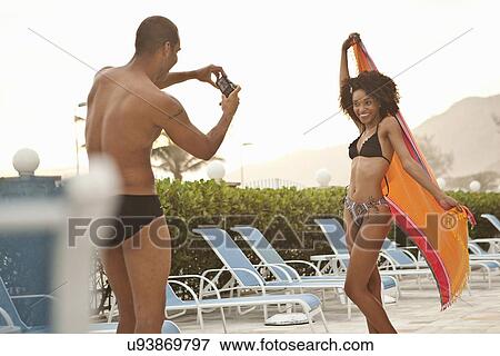 Stock Photo - "Young woman being photographed by boyfriend at hotel poolside, Rio De Janeiro, Brazil". Fotosearch