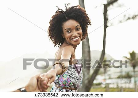 Stock Image - "Young woman holding boyfriends hand at beach, Rio De Janeiro, Brazil". Fotosearch