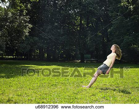 Stock Photograph - Young woman in park free falling backwards with eyes closed. Fotosearch