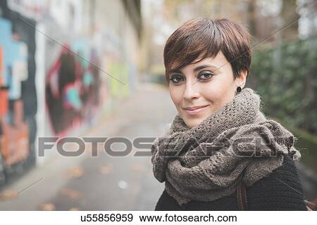Stock Photo - "Young woman on street, graffiti wall in background". Fotosearch