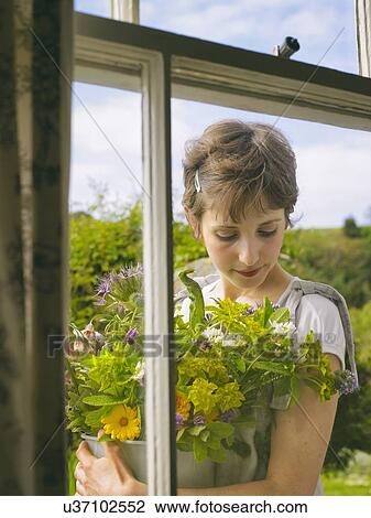 Stock Image - Young woman outside window with a bowl of wildflowers. Fotosearch