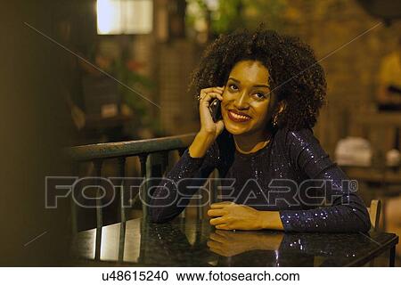 Stock Image - "Young woman sitting at table at bar, using mobile phone". Fotosearch