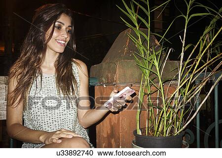 "Young woman sitting outdoors at night, holding smartphone" View Large Photo Image Stock Image - "Young woman sitting outdoors at night, holding smartphone". Fotosearch
