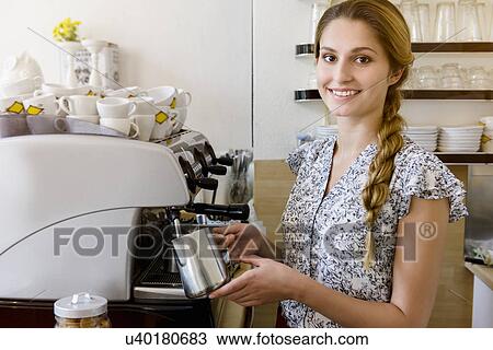 Stock Image - "Young woman using coffee maker looking at camera, portrait". Fotosearch